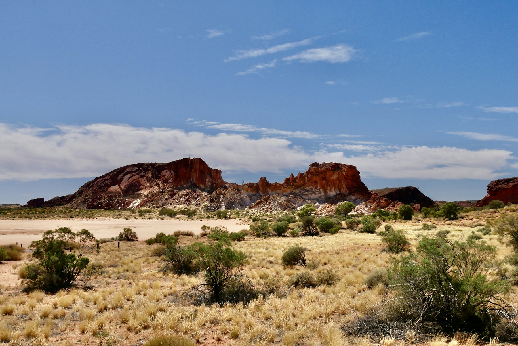 Open Australian bushland with red rock ridges, dry grass and scattered scrub.